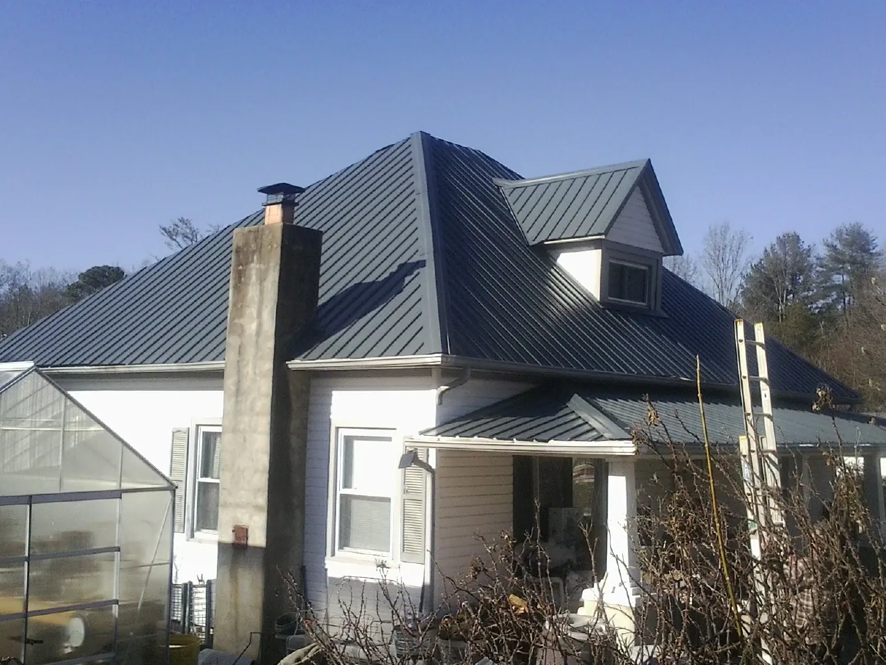Dark blue standing seam metal roof on a white farmhouse with dormer in Villisca