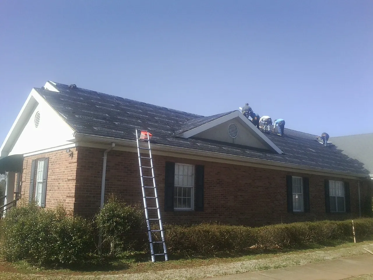 Crew tearing shingles off a brick ranch roof with a ladder set — Emergency Roof Repair work by our crew in Villisca