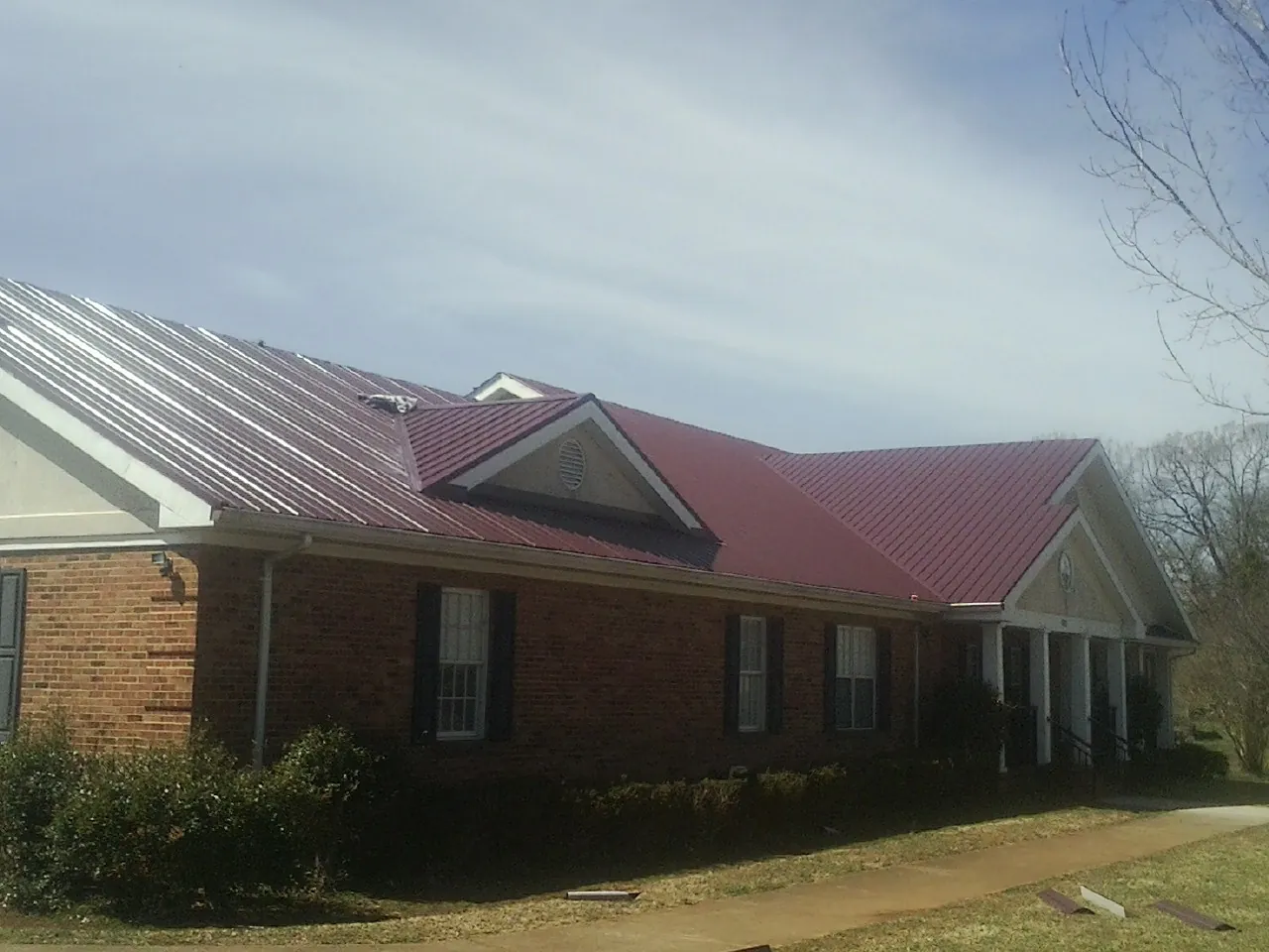 Red metal roof with gabled entries on a long brick building, from a Hail Damage Roof Repair job in Villisca