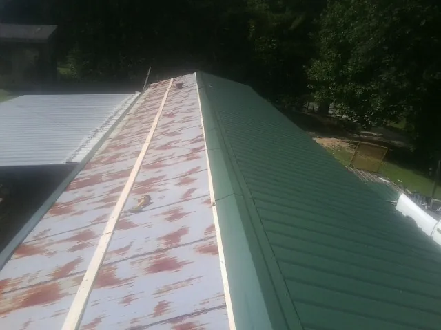 Old rusted panels beside newly installed green metal roofing — Wind Damage Roof Repair by Roofing Brothers in Villisca
