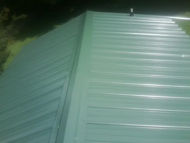 New green metal panels meeting at the ridge of a roof — Flat Roof Repair work by our crew in Villisca