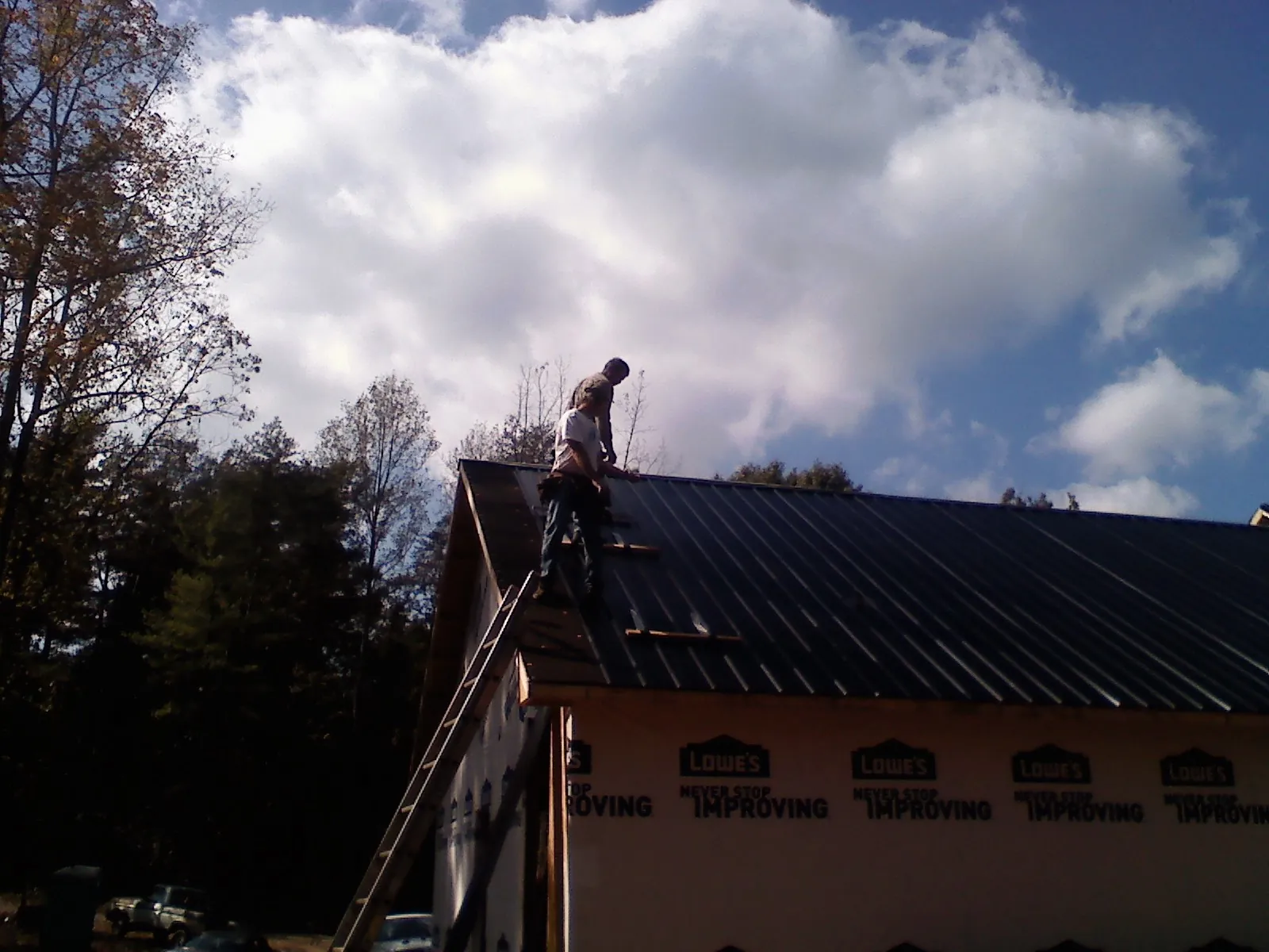 Roofer fastening dark metal panels high against a cloudy sky, from a Roof Inspection job in Villisca