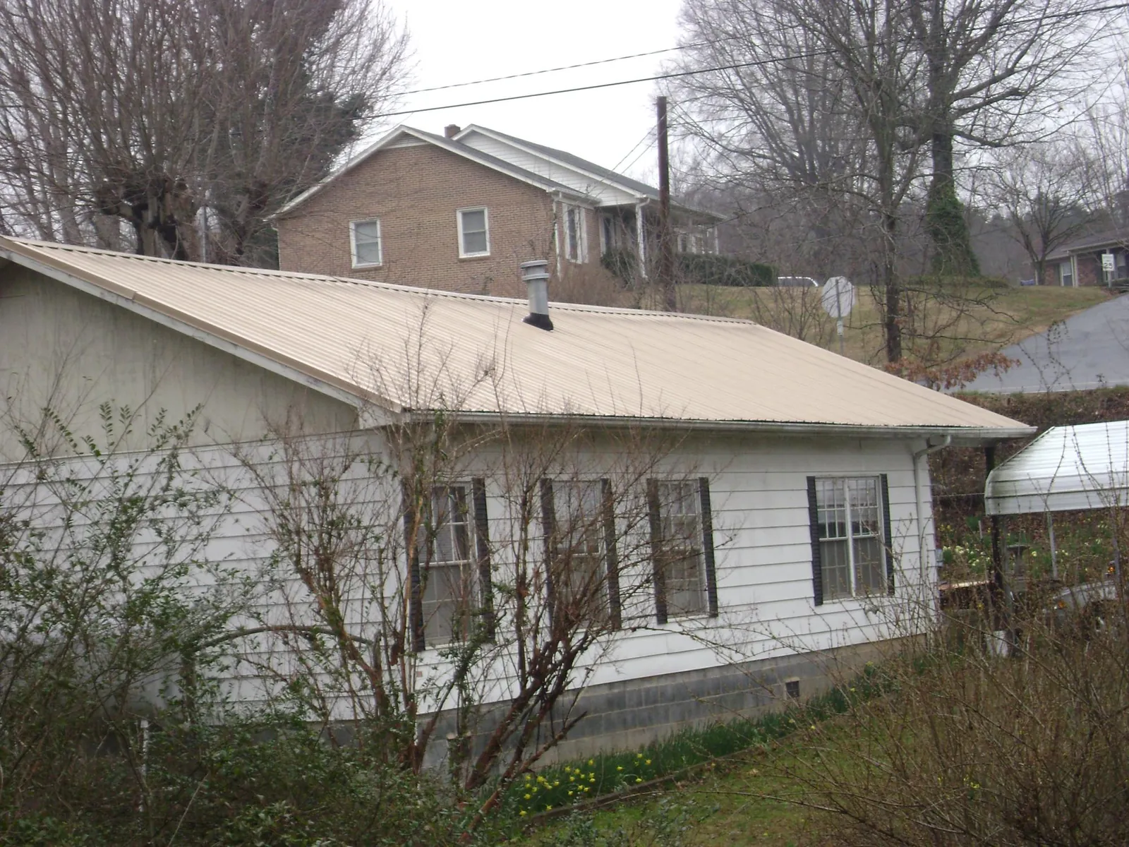 Tan metal roof on a white sided house set into a hillside — Commercial Roofing by Roofing Brothers in Villisca